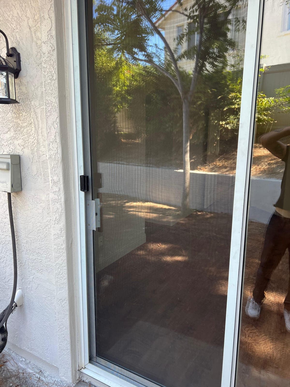 A sliding screen door fitted in its white frame beside a stucco wall.