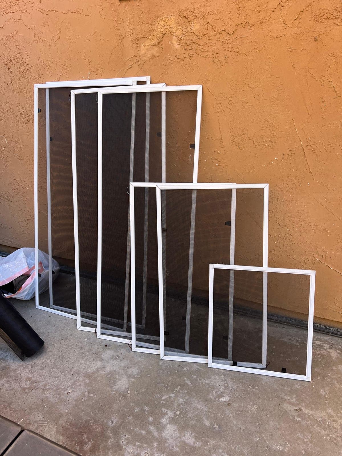 A set of new screens, tall to small, leaning against an orange stucco wall.