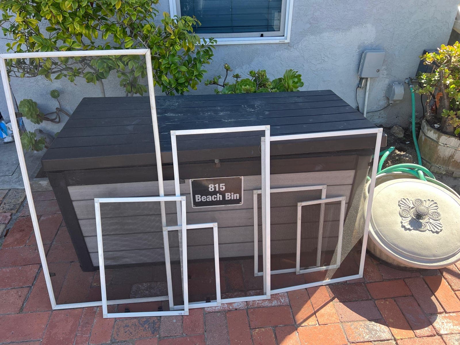 New screens in white frames propped against a storage bin on a brick patio.
