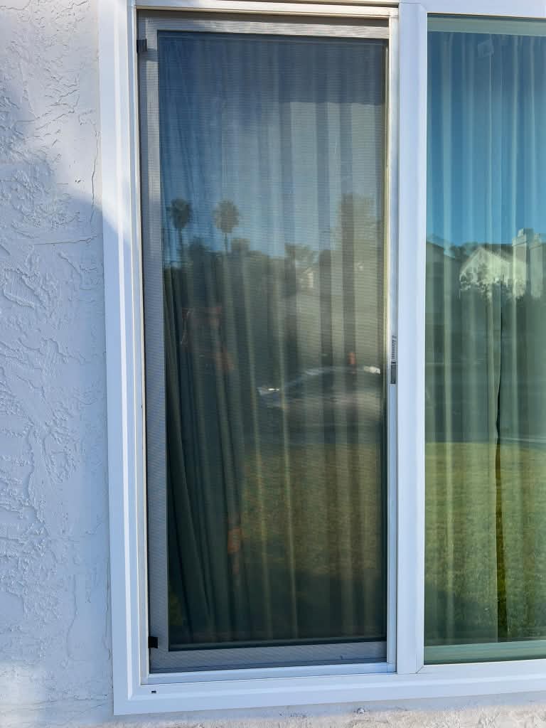A new window screen installed on a tall sliding window of a white stucco home by Screenova Solutions.