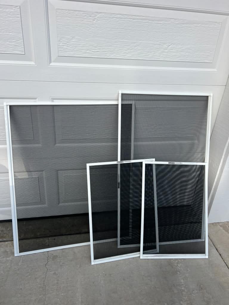 Four replacement window screens with white frames leaning against a white garage door.