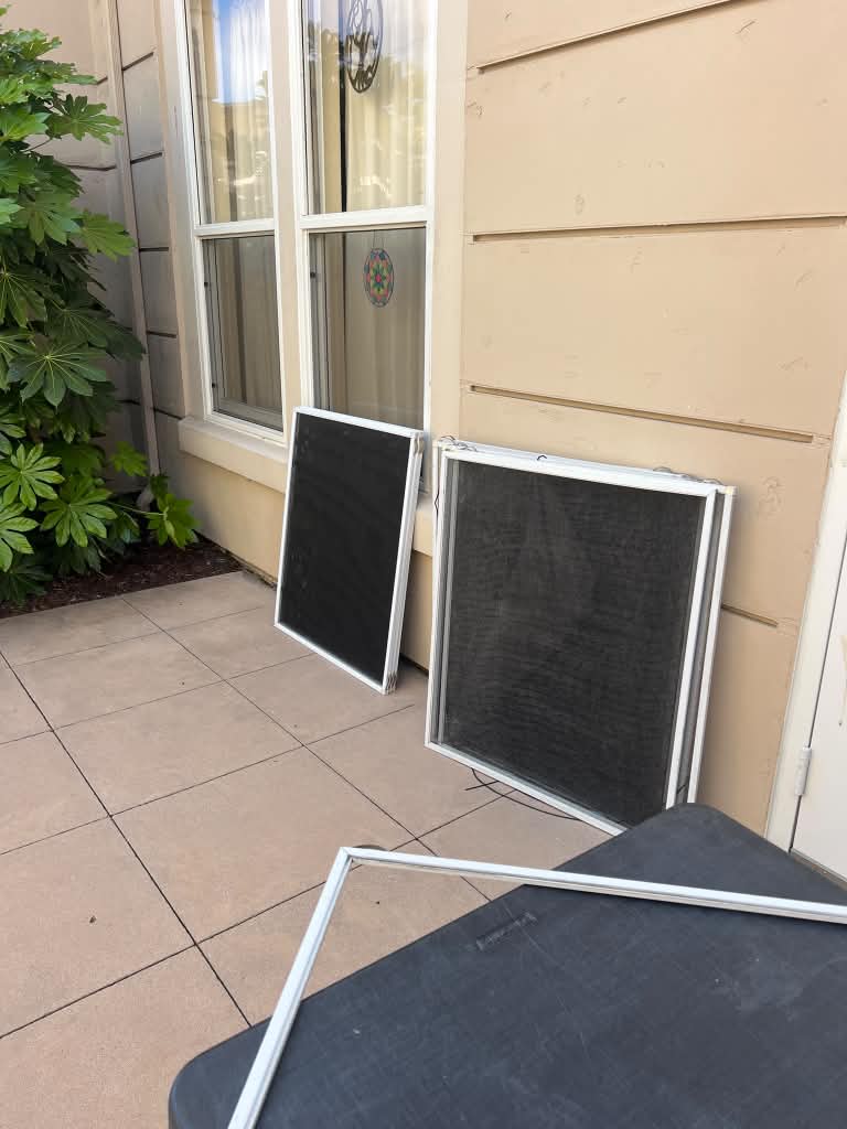 Window screens being rescreened on a home patio, with an empty screen frame on a work table in the foreground.