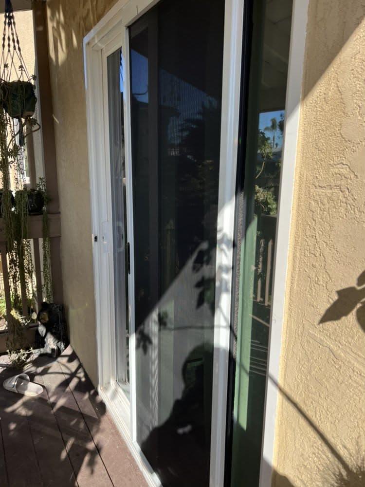 A newly installed sliding patio screen door on a sunny balcony with hanging plants.