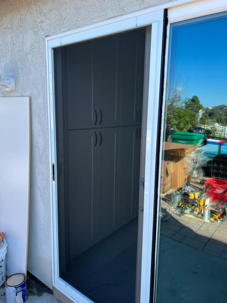 A newly installed sliding screen door with dark mesh and a white frame on a patio door, installed by Screenova Solutions.