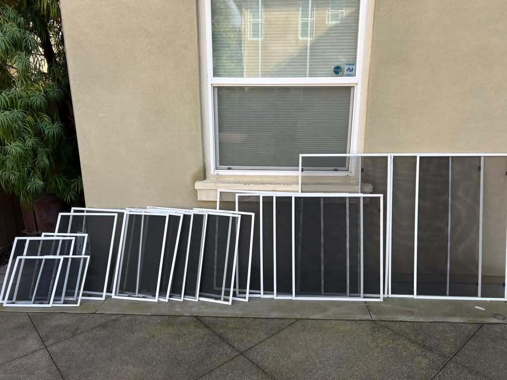 A full set of new white window screens lined up along a beige stucco house during a whole-house window screen replacement by Screenova Solutions.