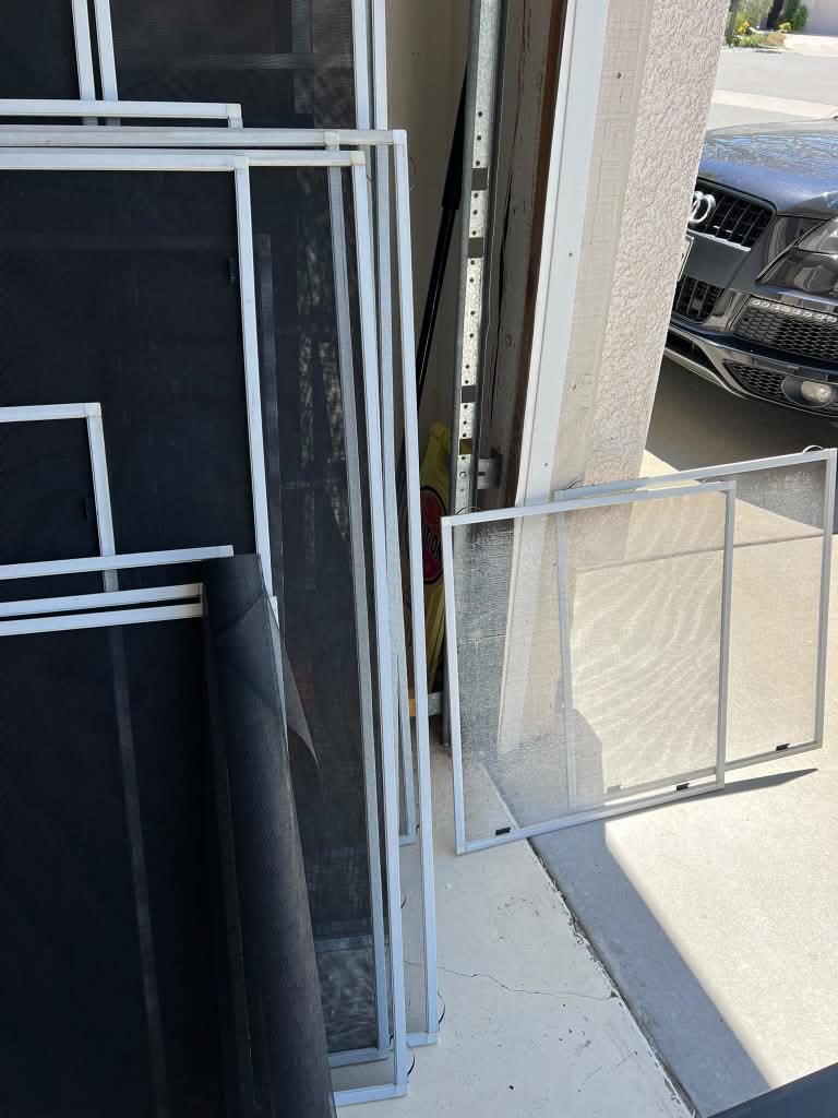 Window screen frames and a roll of screen mesh in a garage alongside an old faded screen awaiting rescreening.