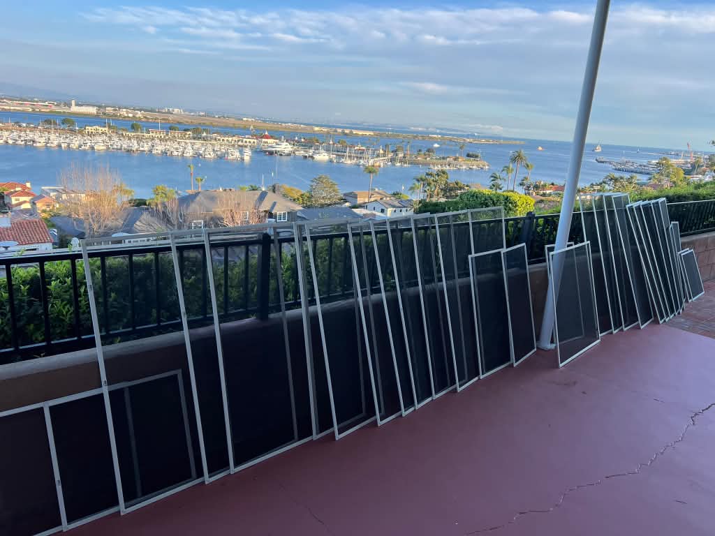 Over twenty new white-framed window screens from Screenova Solutions lined up on a hillside balcony overlooking the bay and its marinas.