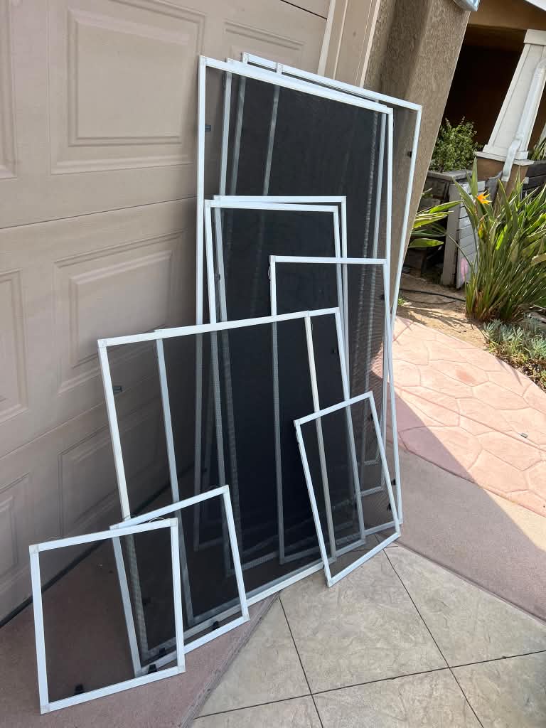 Window screens in various sizes arranged from largest to smallest against a tan garage door, custom-made by Screenova Solutions.
